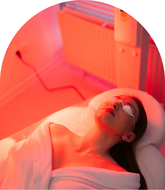 Person lying under red light therapy wearing protective eyewear, wrapped in a towel.