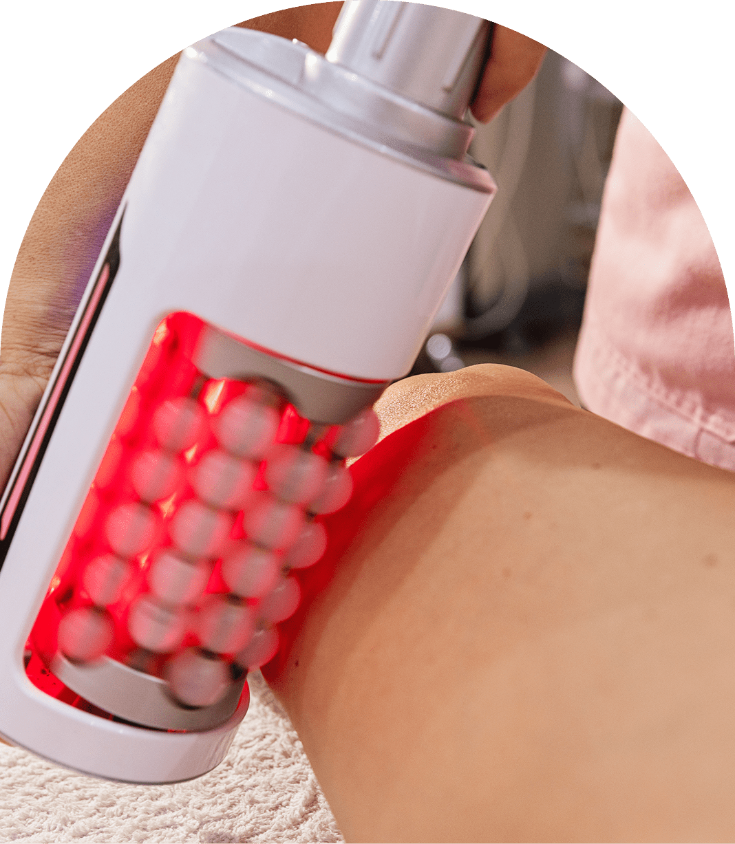 A person uses a handheld device emitting red light on their skin.