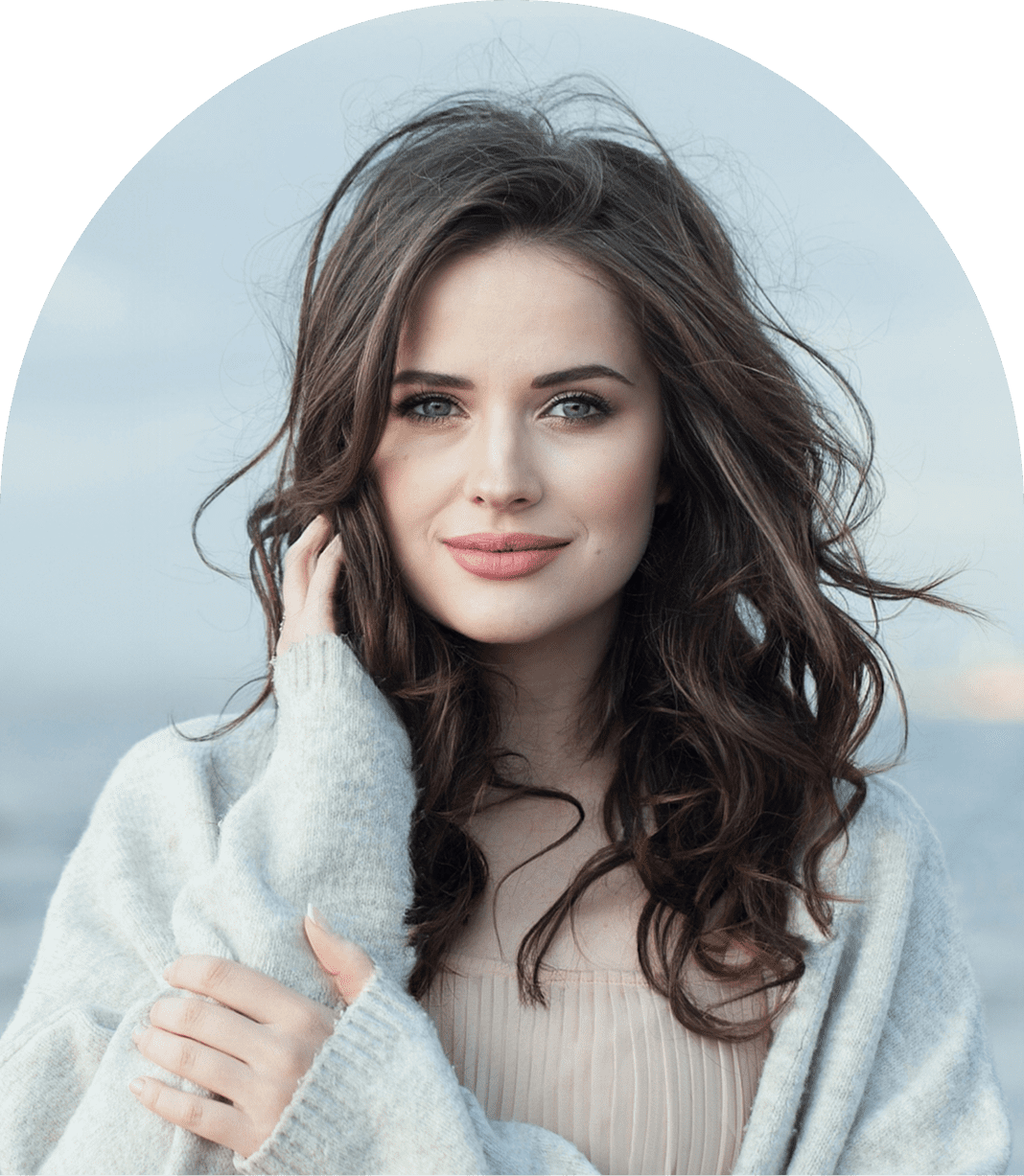 A woman with long brown hair and a soft smile stands outdoors, wearing a light sweater. The background features a blurred, natural setting.