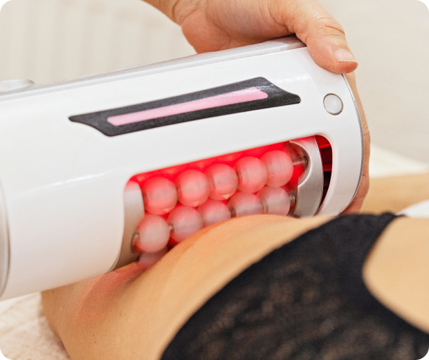 A person uses a red light therapy massager with rollers on someone's abdomen.