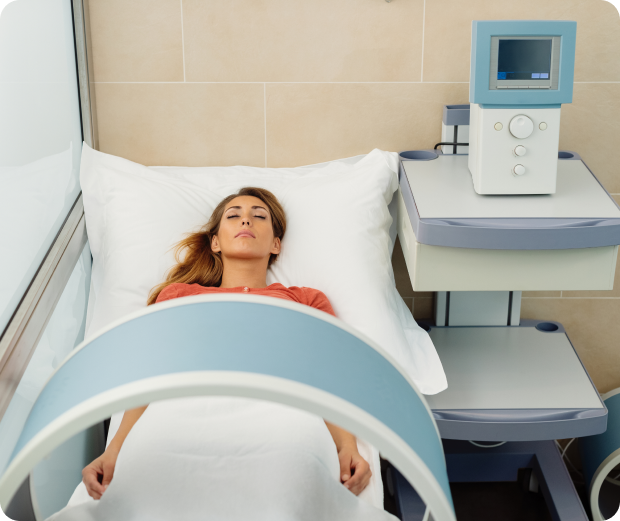 A woman is lying in a hospital bed with medical equipment beside her and a large arch over the bed.