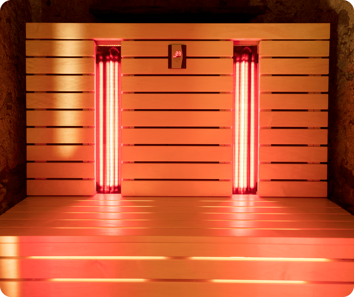 Infrared sauna interior with wooden benches, two vertical heaters emitting red light, and a central digital temperature display showing 23 degrees.